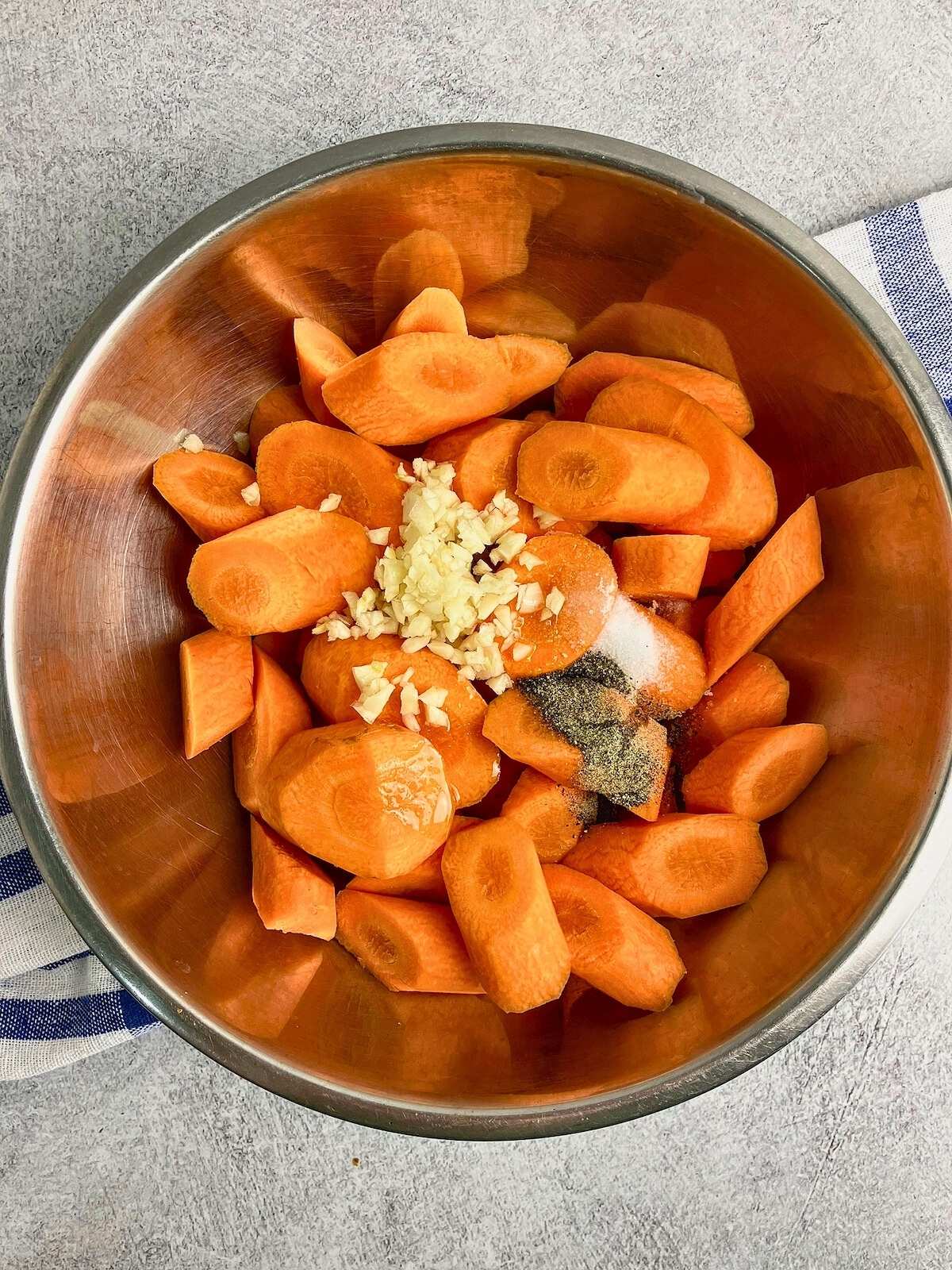 Sliced carrots in a mixing bowl with chopped garlic, olive oil, and seasonings.