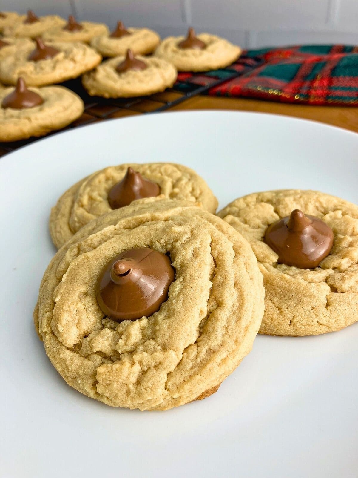 Peanut butter blossoms on a white plate next to a cooling rack of cookies.