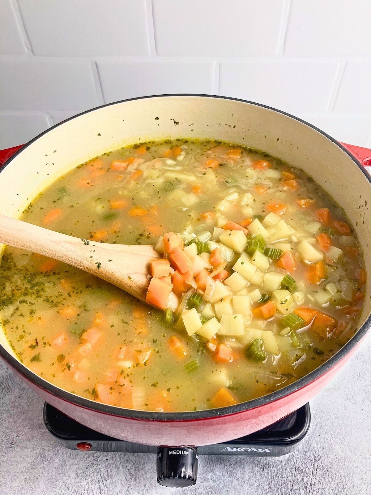 A wooden spoon is used to lift out some of the cooked vegetables in the soup before pureeing.