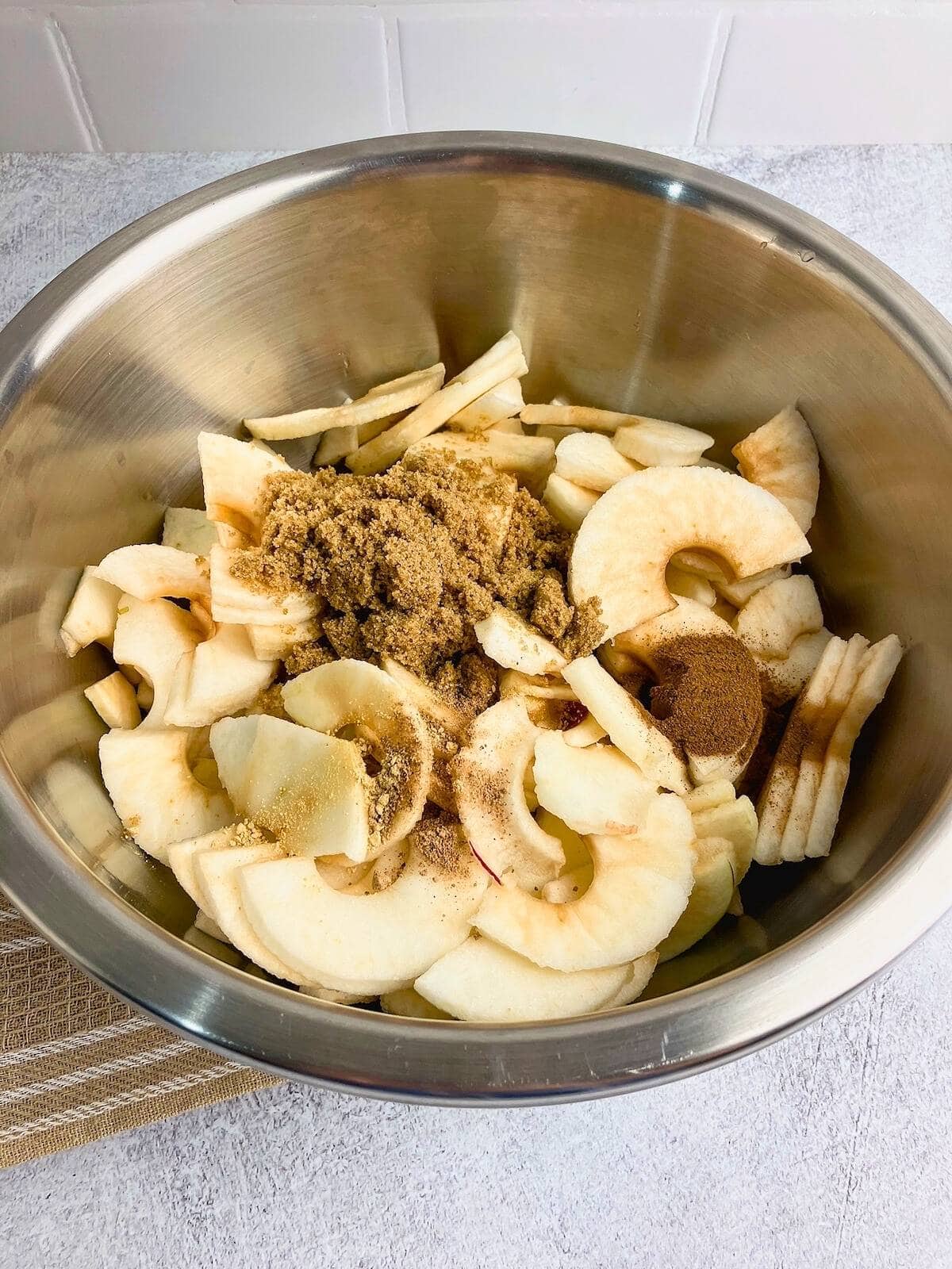 Sliced apples in a large mixing bowl with brown sugar and spices.