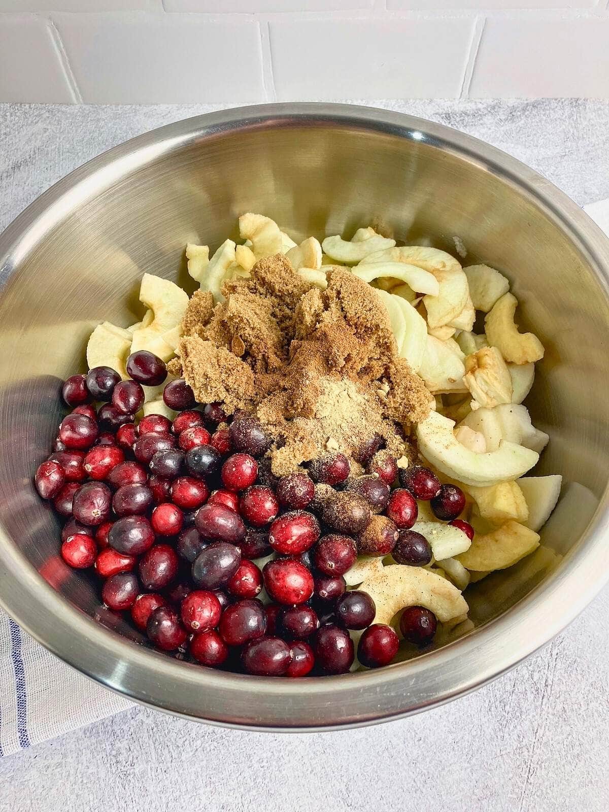 Brown sugar and spices were added to the bowl of apples and cranberries.