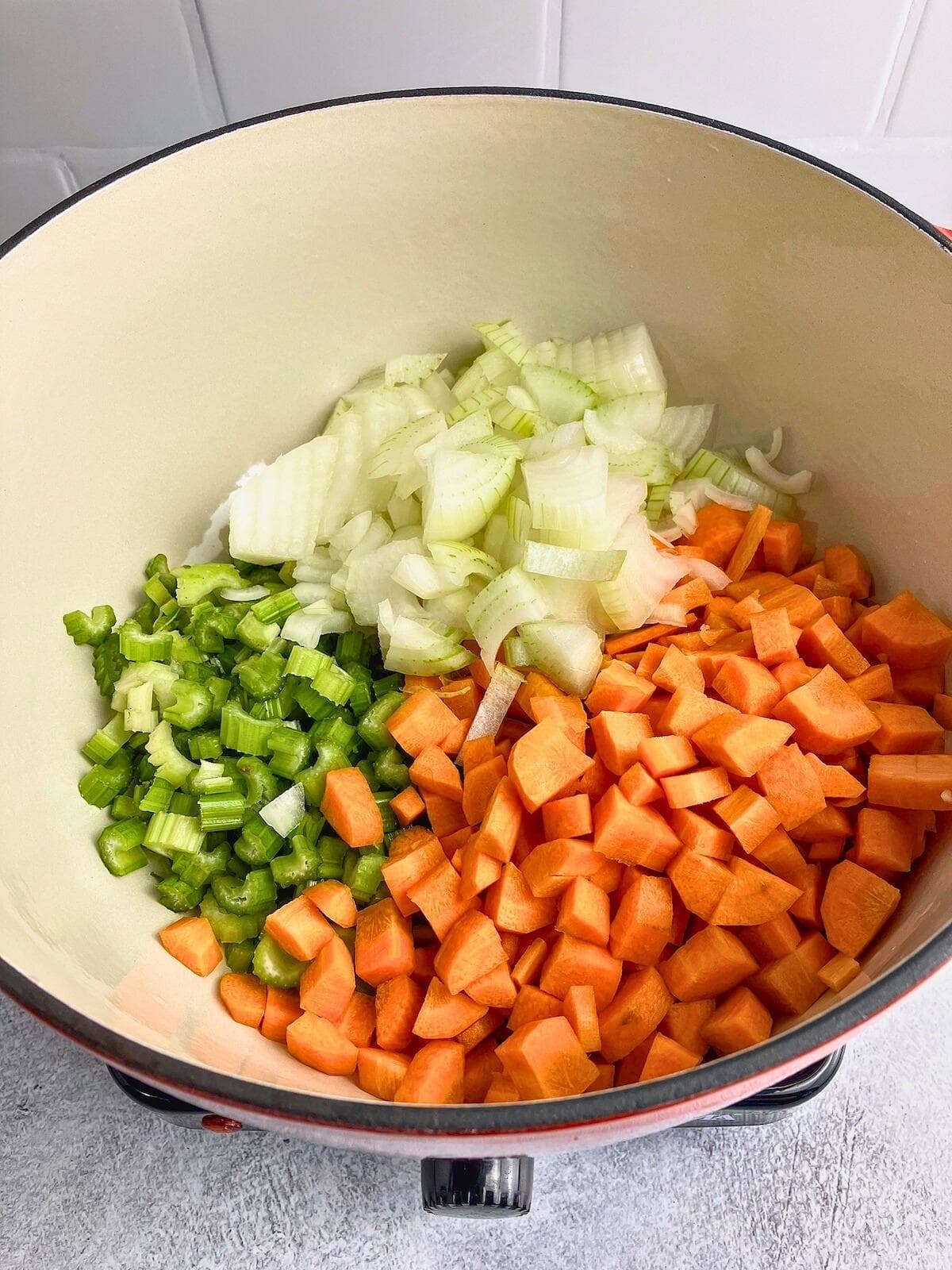 A red dutch oven with diced celery, carrots, and onions in it.