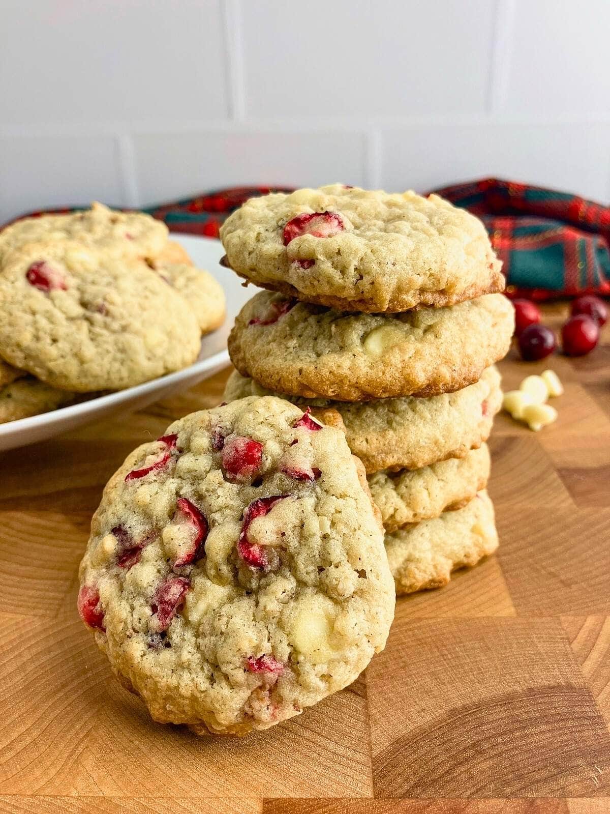 Homemade white chocolate cranberry oatmeal cookies on a wooden table next to a platter.
