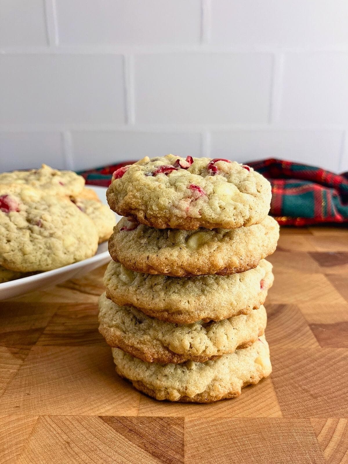 Cranberry white chocolate chip oatmeal cookies stacked up next to a platter of cookies.