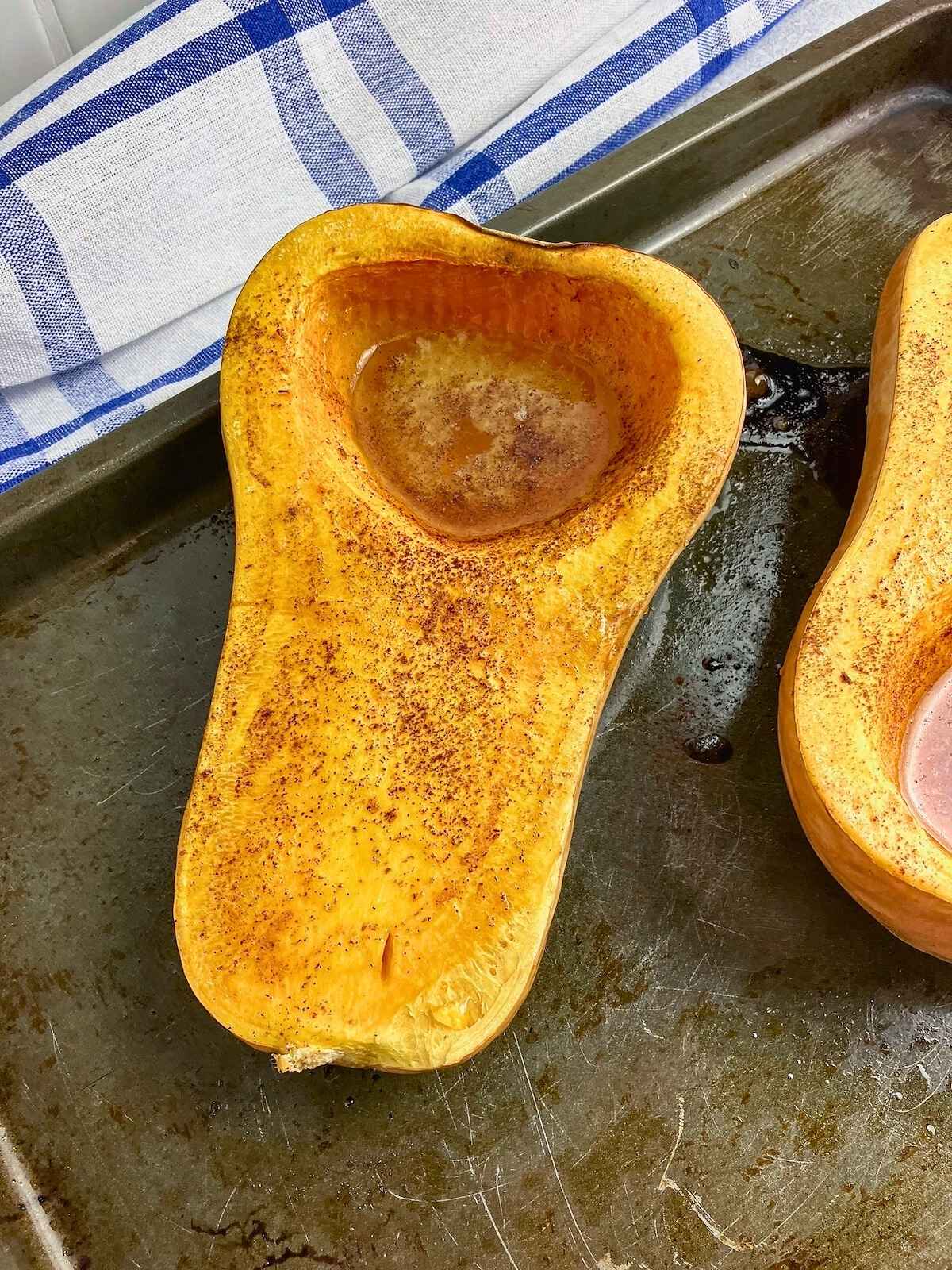 Two halves of whole roasted butternut squash with honey and cinnamon on a baking sheet.