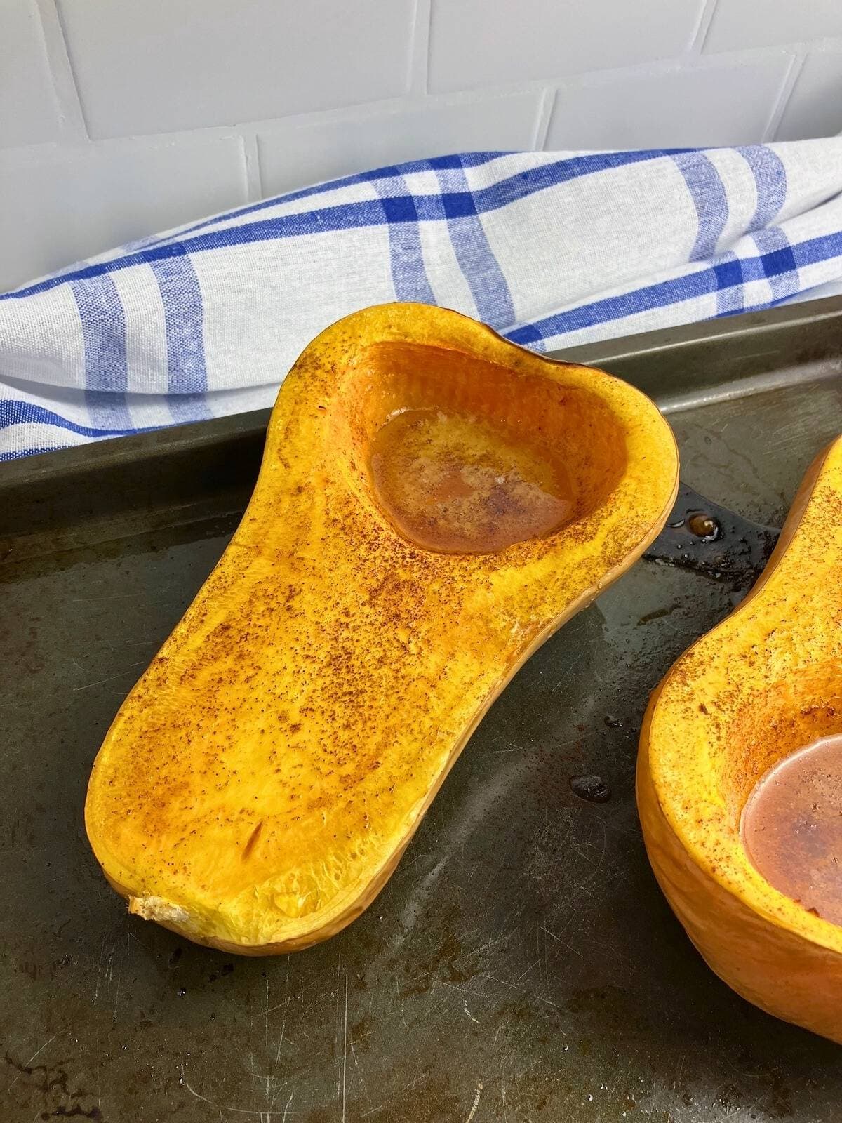 Two halves of whole roasted butternut squash with honey on a baking sheet.