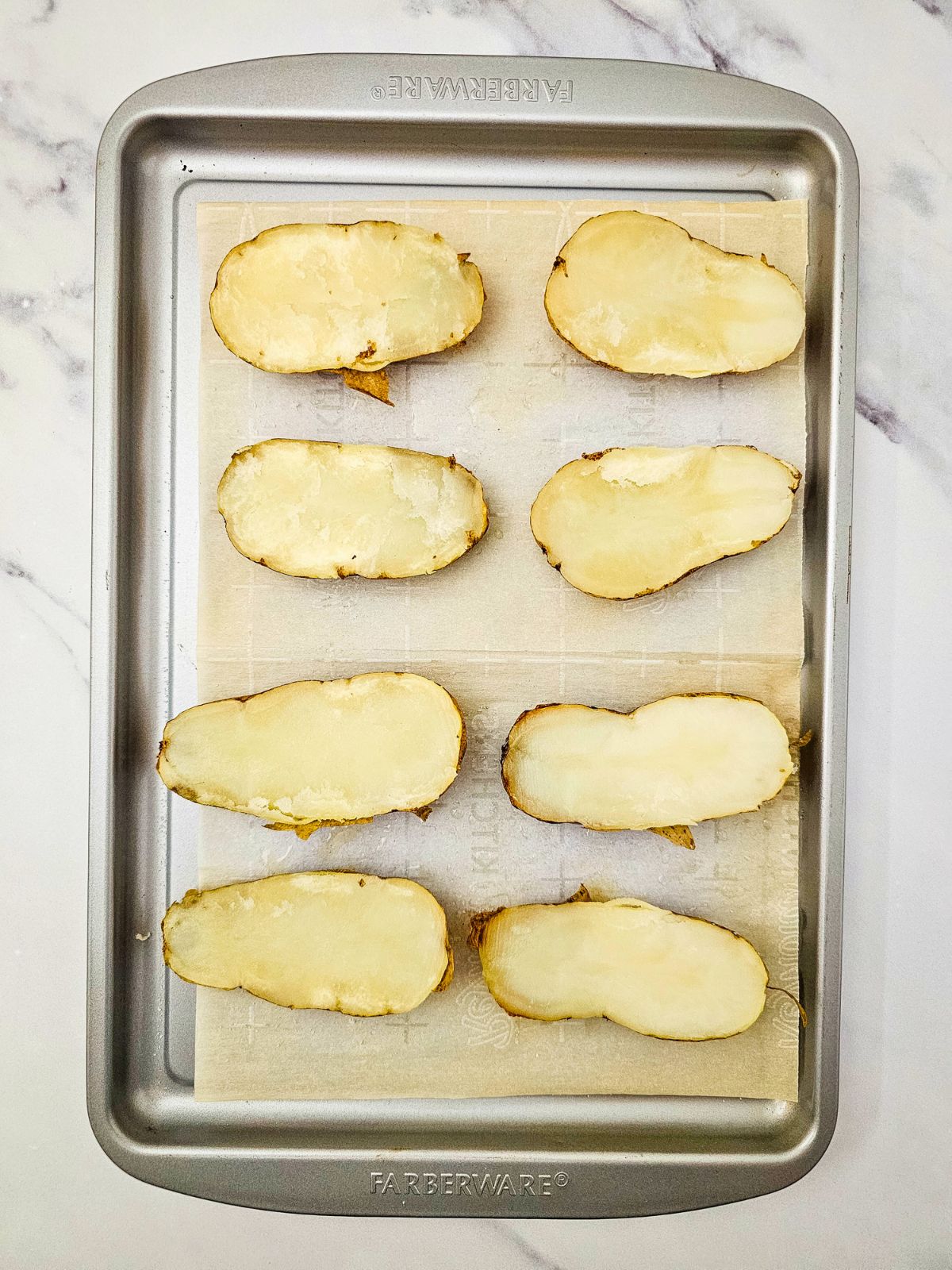 The baked potatoes have been cut in half and placed cut side up on the baking sheet.