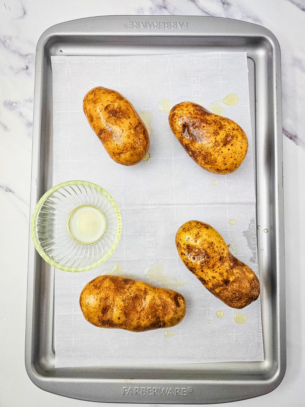 Potatoes on a baking sheet have been basted with olive oil.