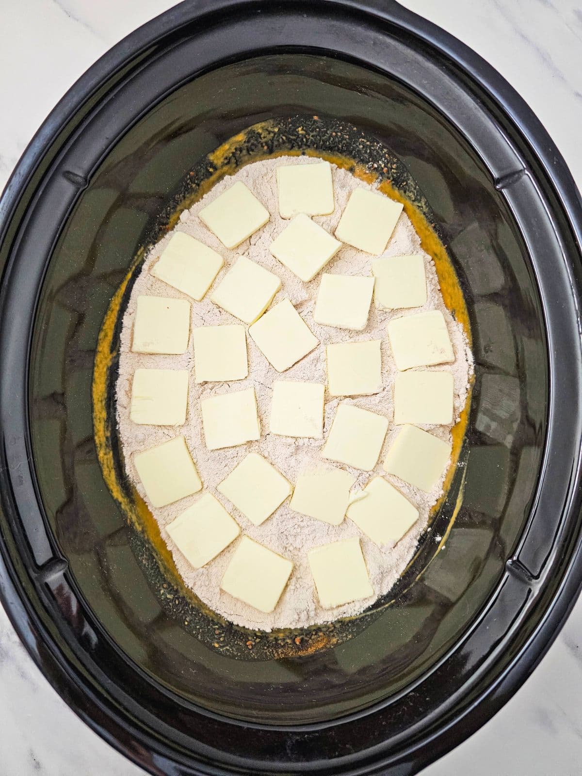 Slices of butter are spread evenly over the top of the cake mix.