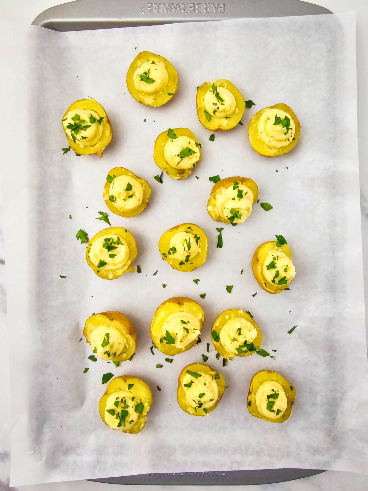 A baking sheet with deviled potatoes filled with filling and topped with freshly chopped parsley.