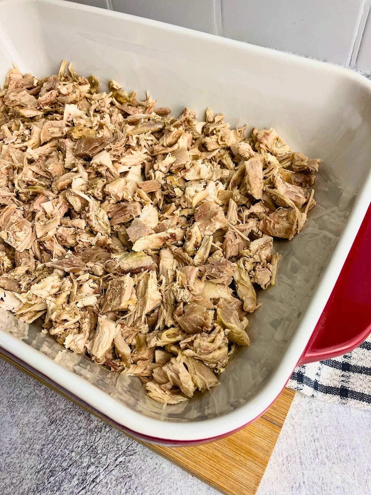 The diced cooked turkey meat has been spread on the bottom of a casserole dish.