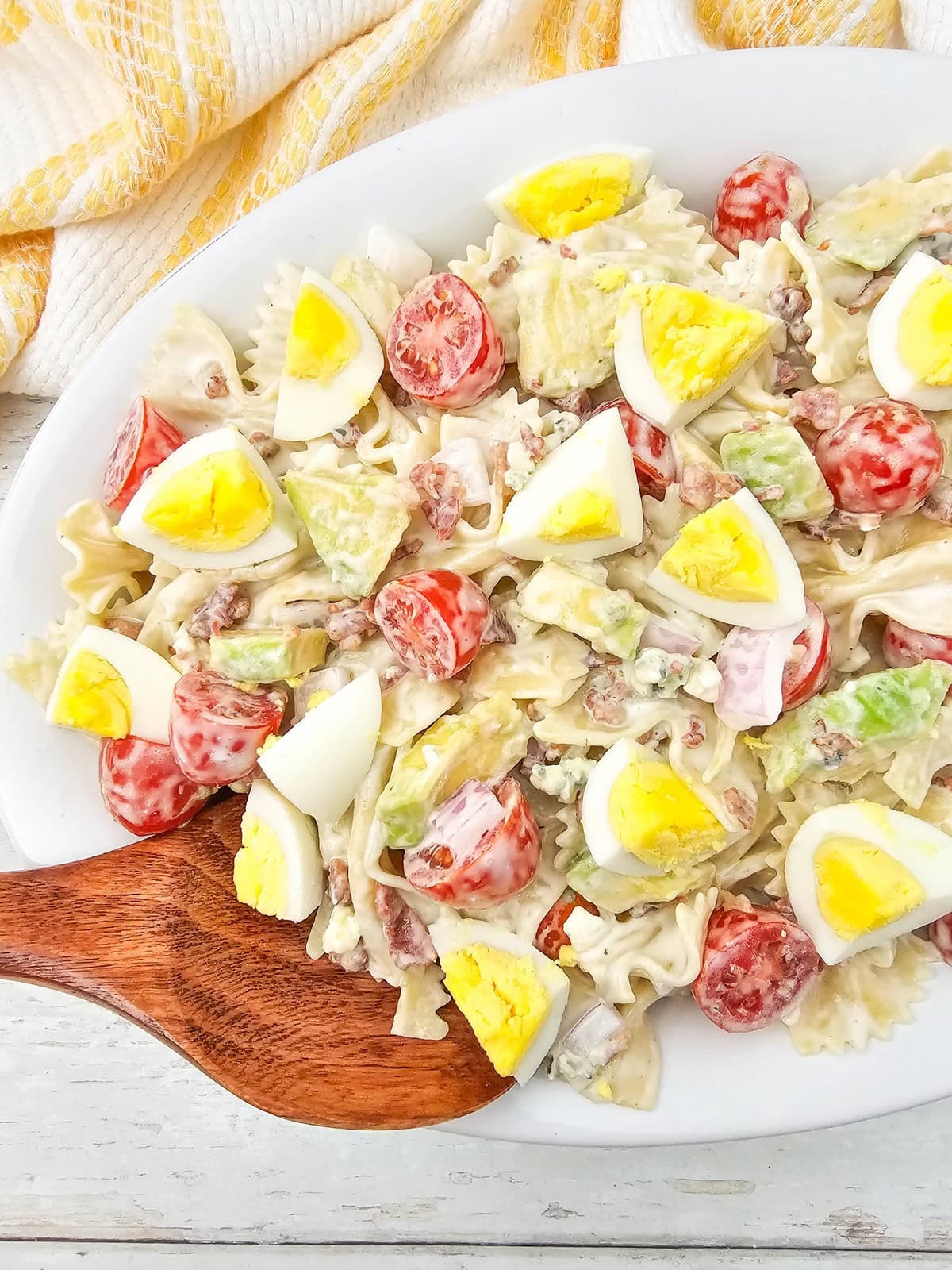 Easy homemade cobb pasta salad on a white serving platter with a wooden spoon.