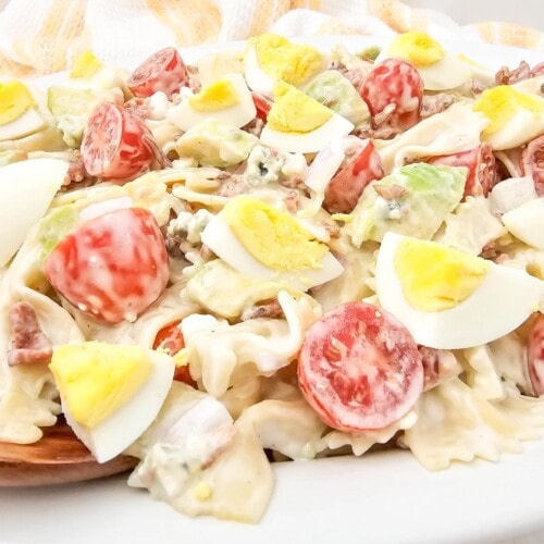 Easy homemade cobb pasta salad on a white serving platter with a wooden spoon.