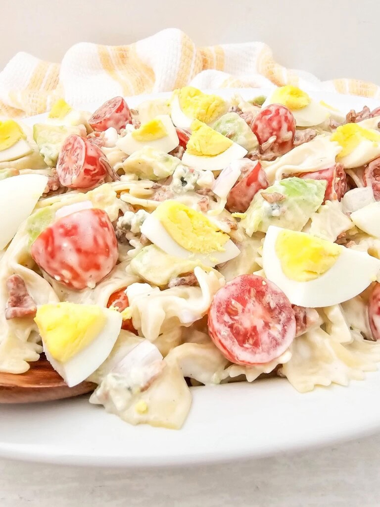 Easy homemade cobb pasta salad on a white serving platter with a wooden spoon.