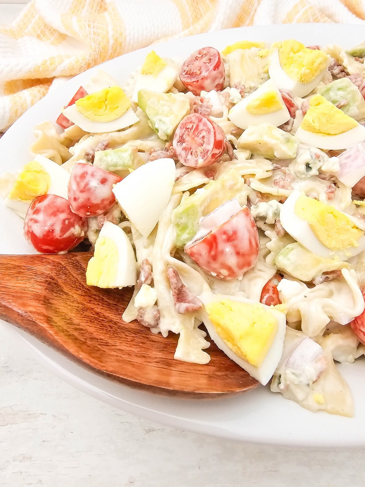 Easy homemade cobb pasta salad on a white serving platter with a wooden spoon.