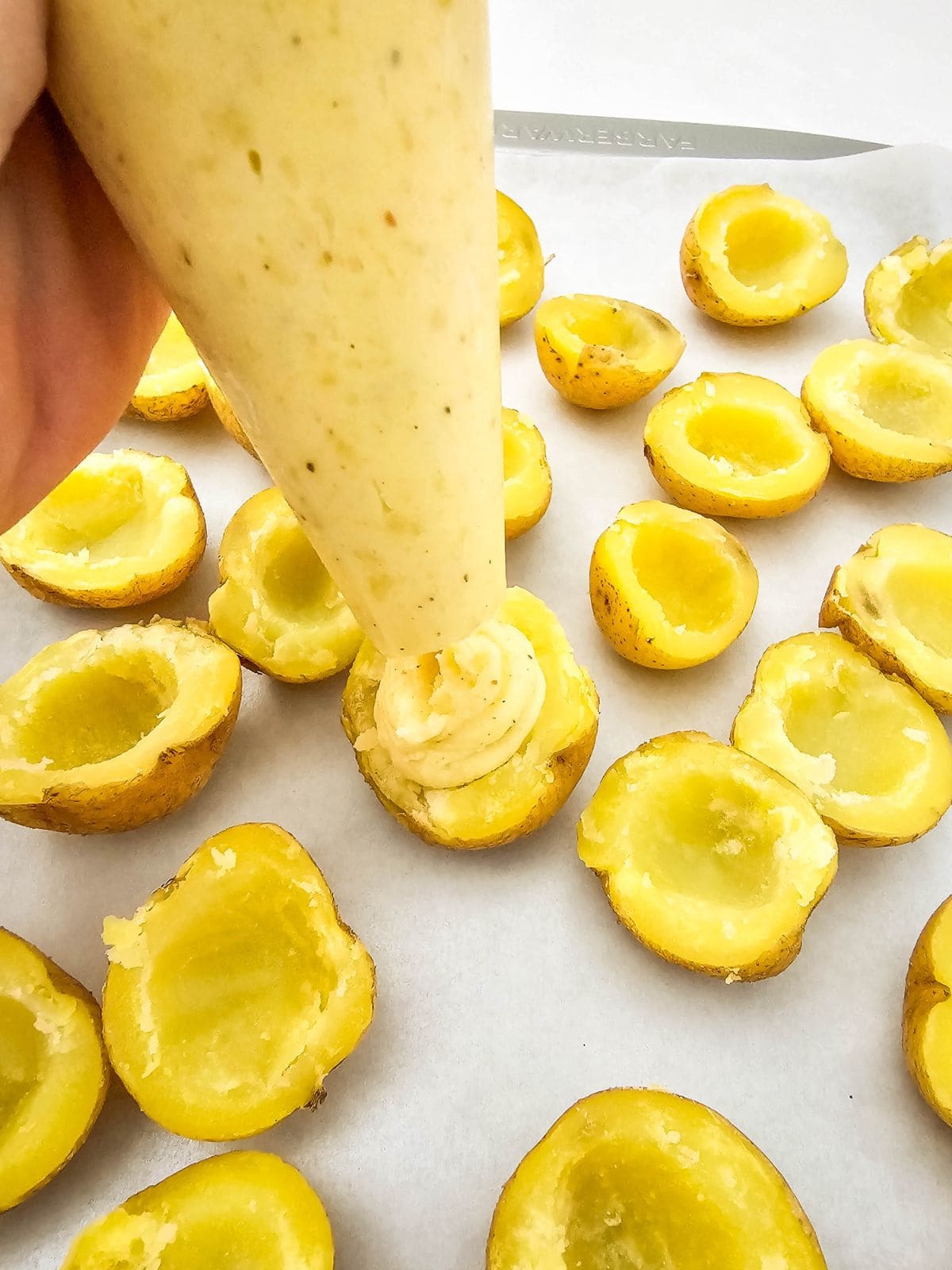 Using a piping bag to fill the hollowed potatoes with the prepared filling.