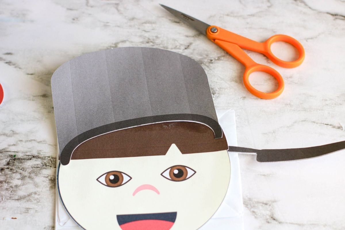 The hat has been glued onto the paper bag puppet's head.