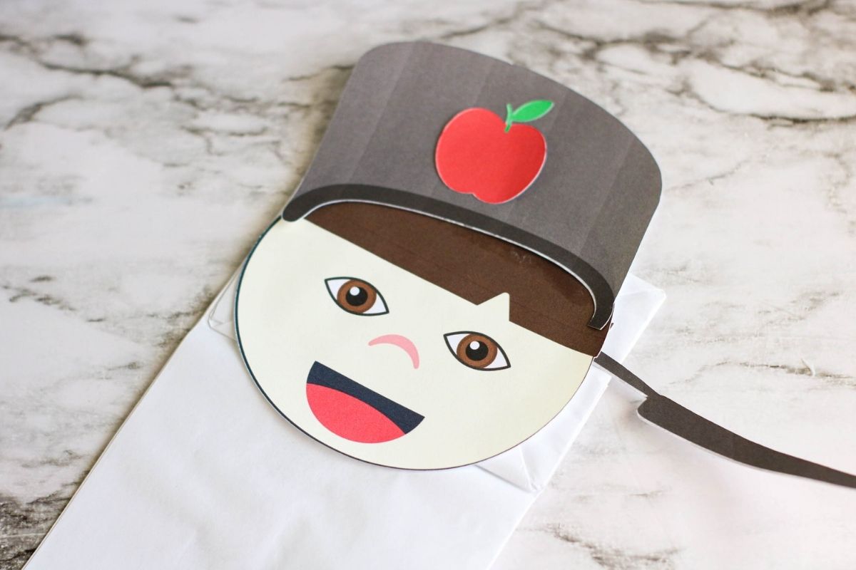 A Johnny Appleseed paper bag puppet laying on top of a marble counter.