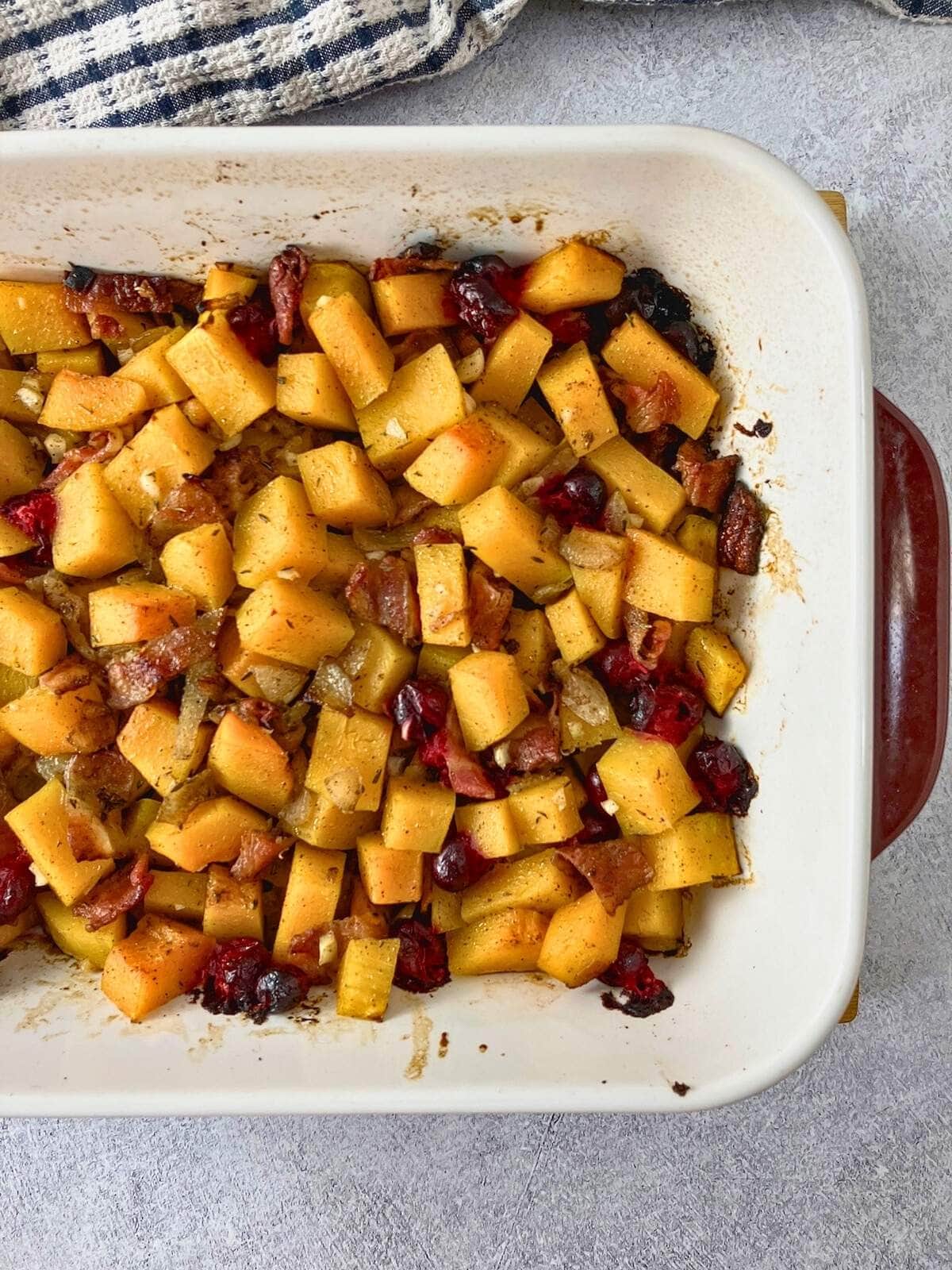 Baked butternut squash casserole with cranberries and bacon cooling on the counter.