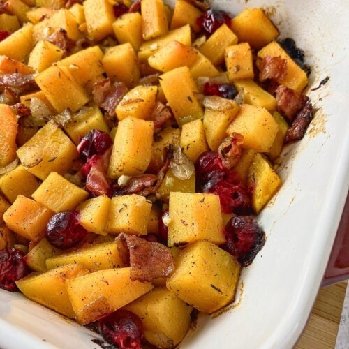 Baked maple bacon butternut squash cranberry casserole in a red and white dish.