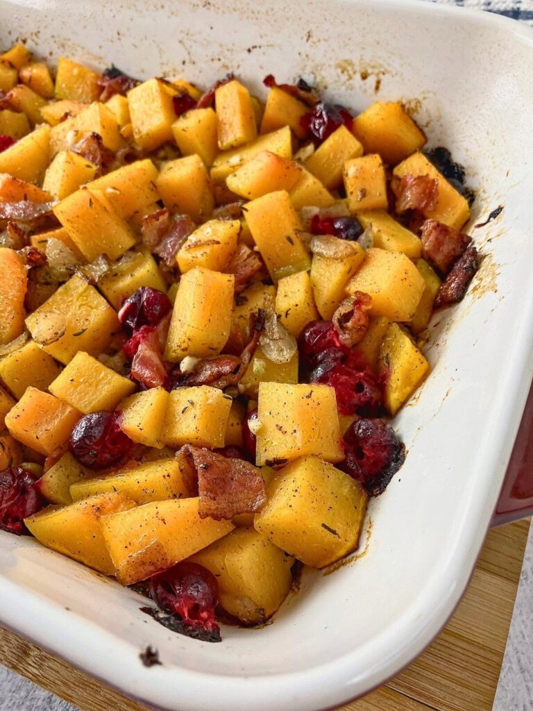 Baked maple bacon butternut squash cranberry casserole in a red and white dish.