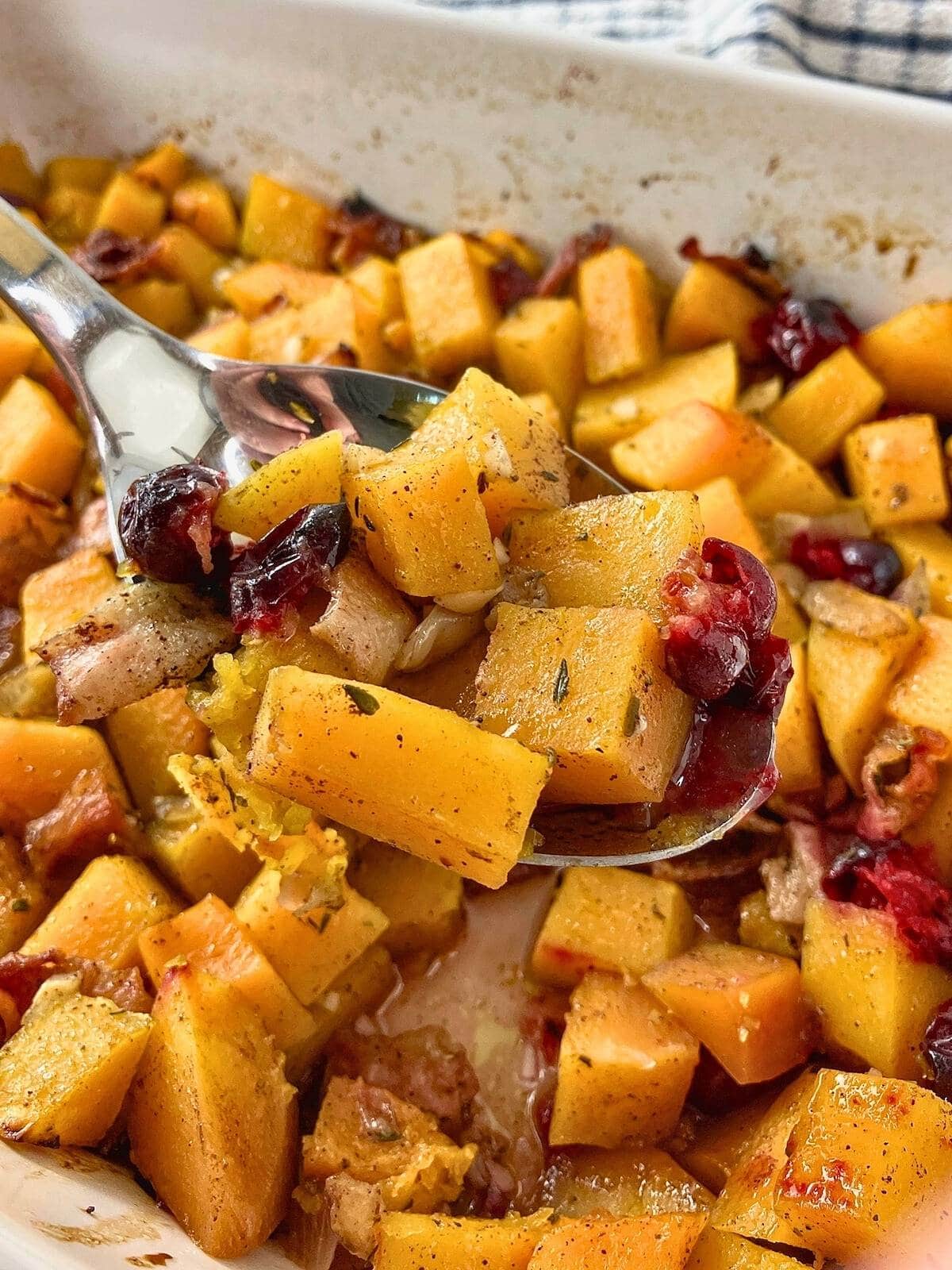 Lifting up a serving spoon of maple bacon butternut squash cranberry casserole.