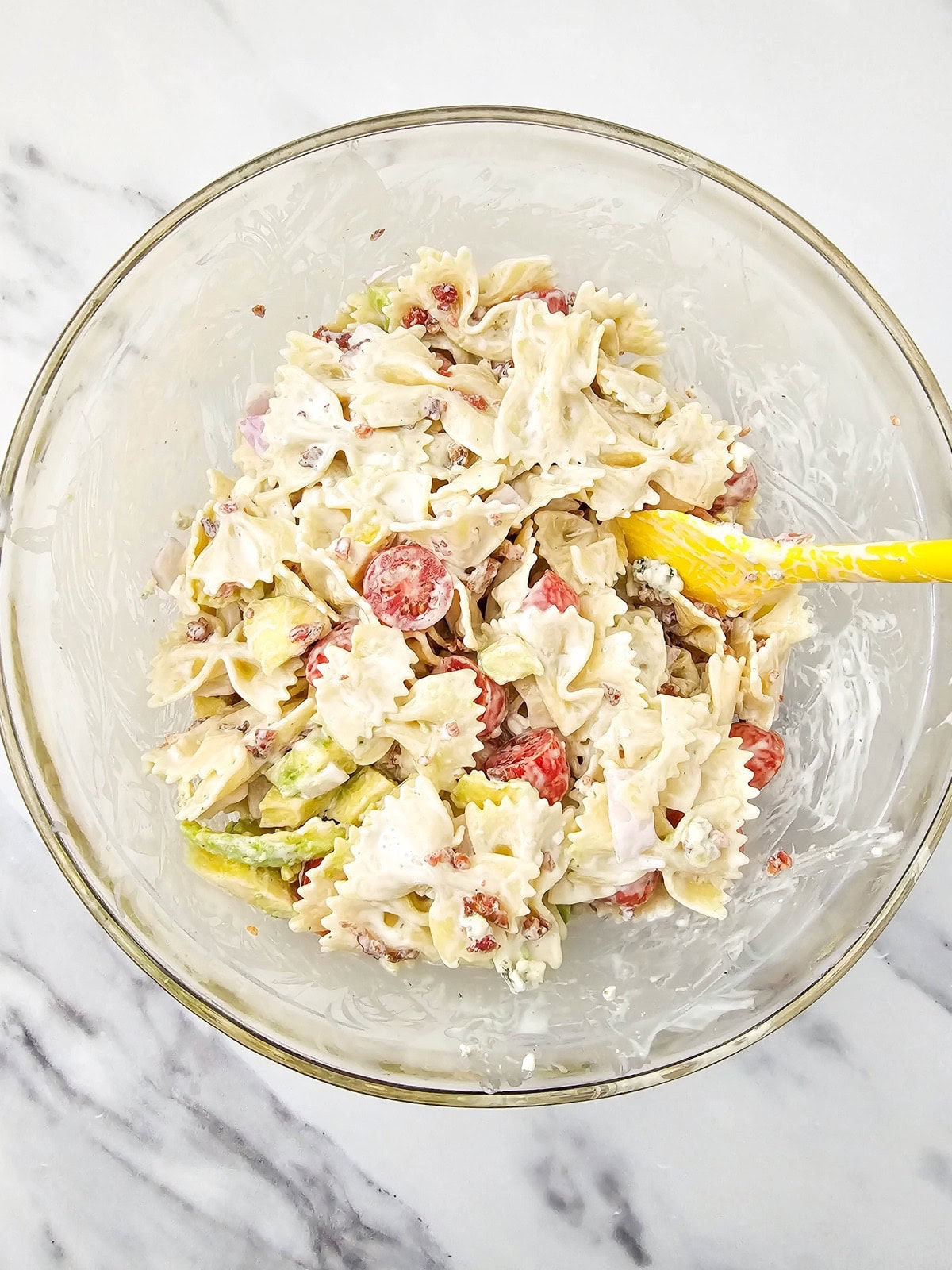 Mixing cobb pasta salad together in a glass mixing bowl.