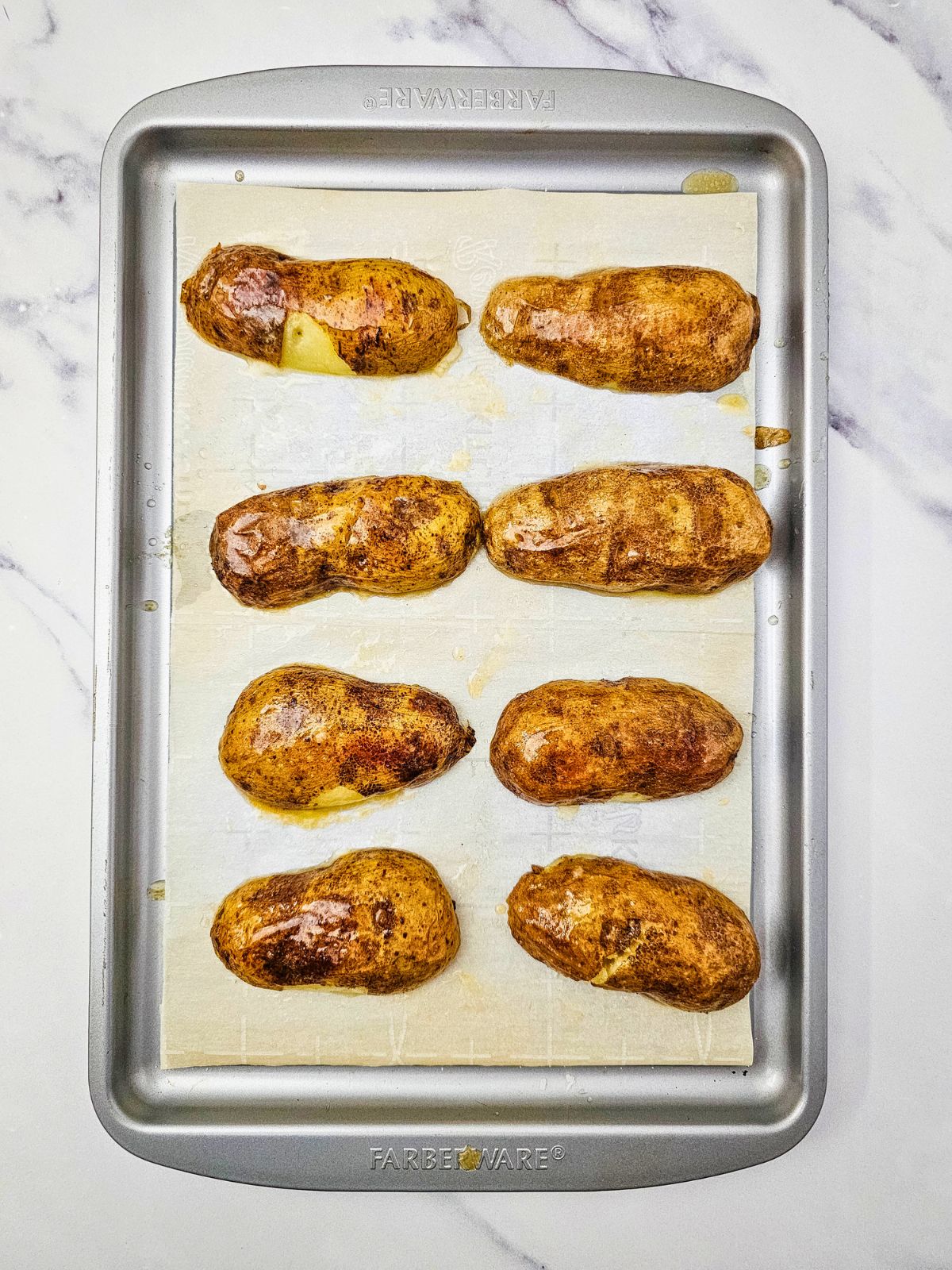 Baked potatoes are cut in half and placed cut side down on a baking sheet.
