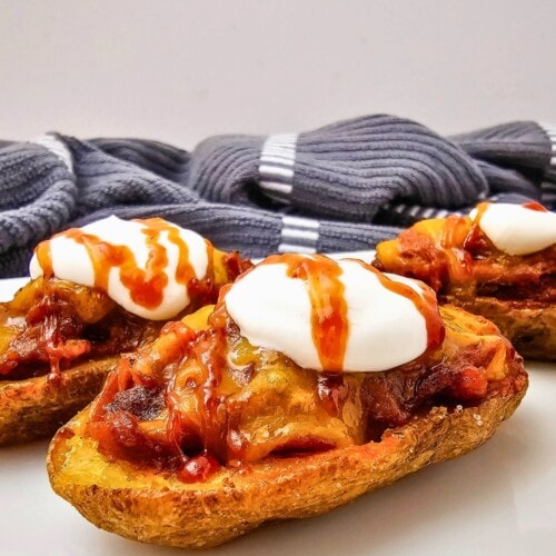 Easy pulled pork potato skins with cheddar cheese, sour cream, and BBQ sauce.