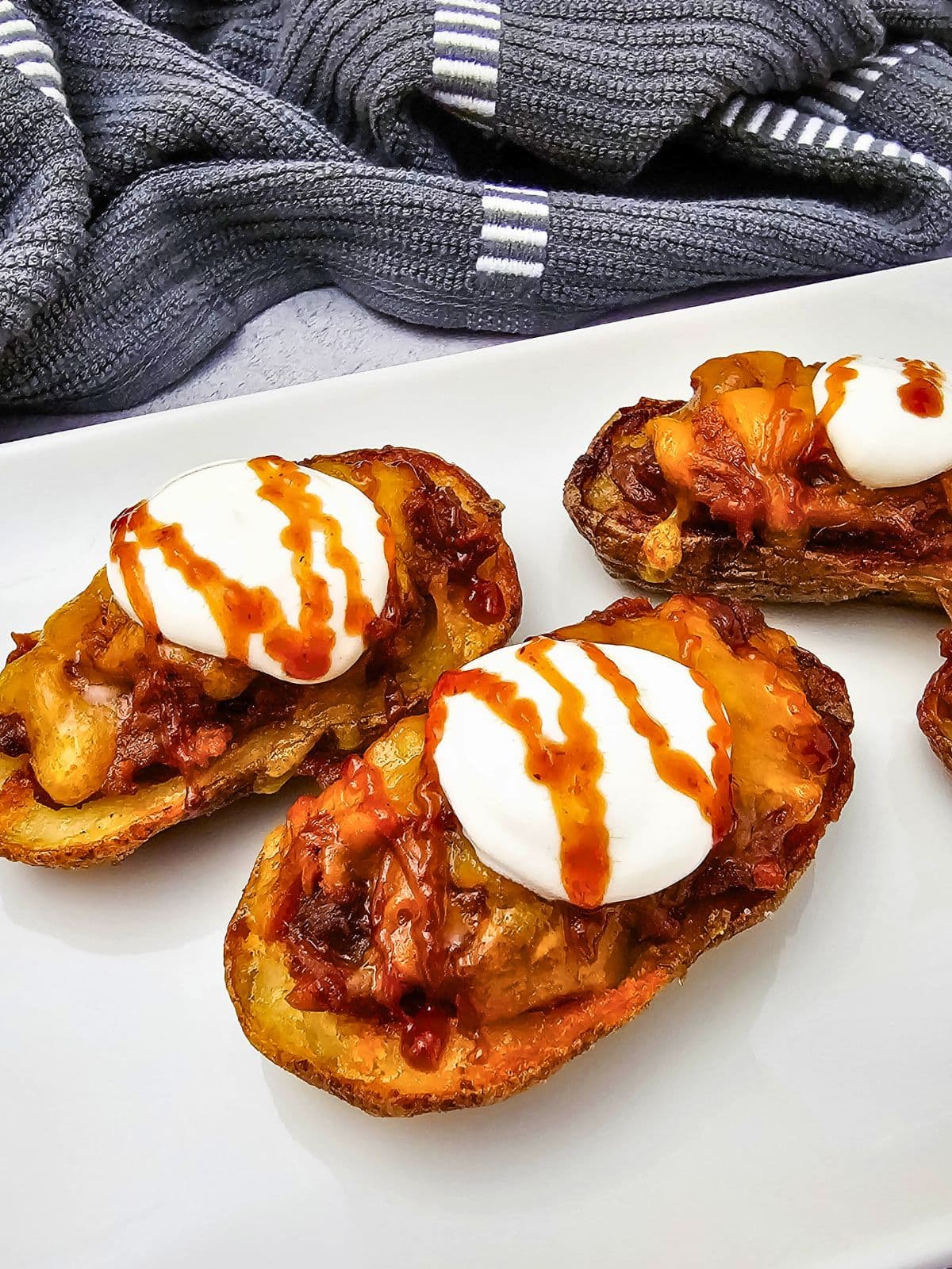 Easy pulled pork potato skins with cheddar cheese, sour cream, and BBQ sauce.