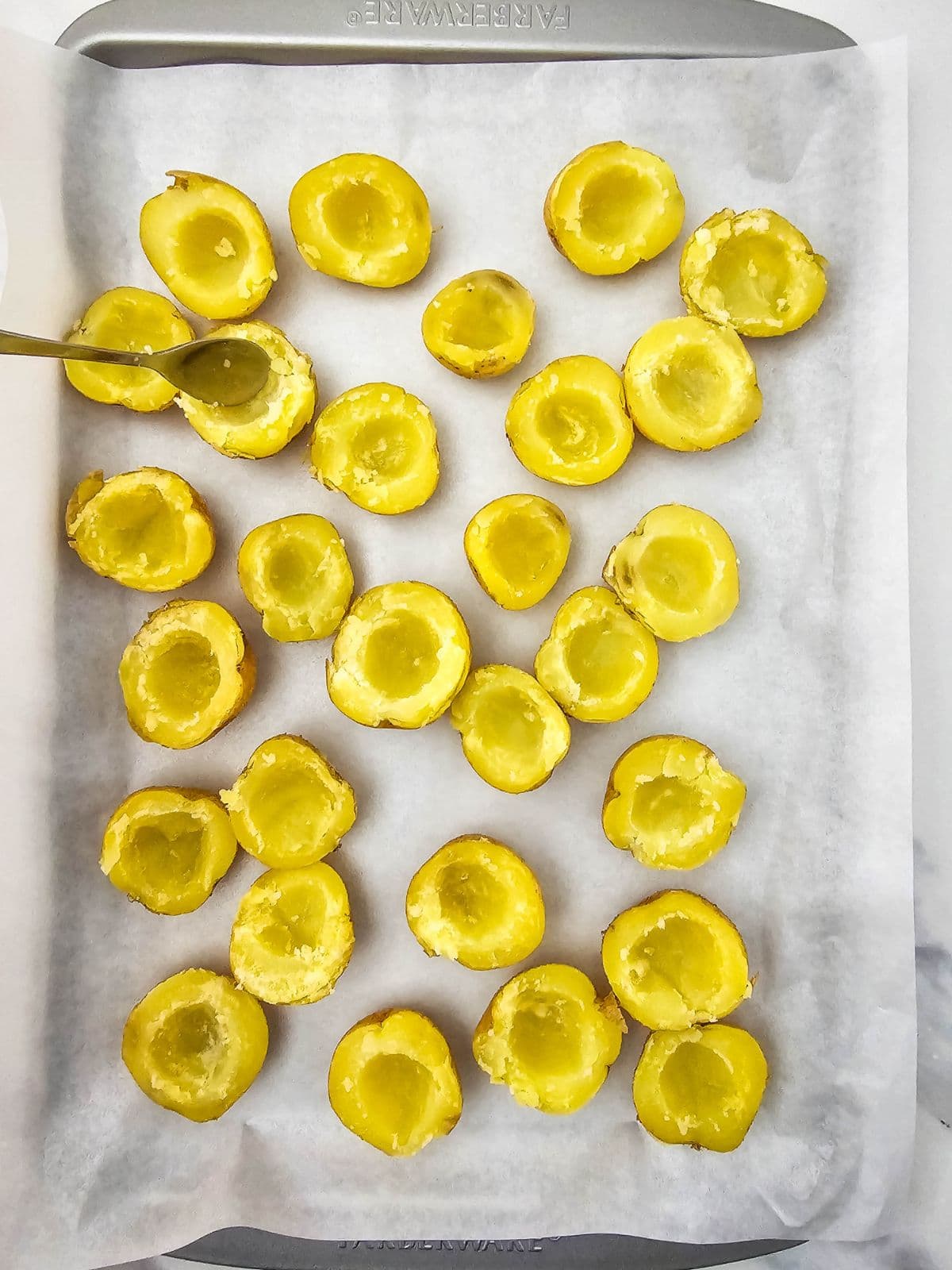 Scooping out the centers of the halved potatoes with a spoon.