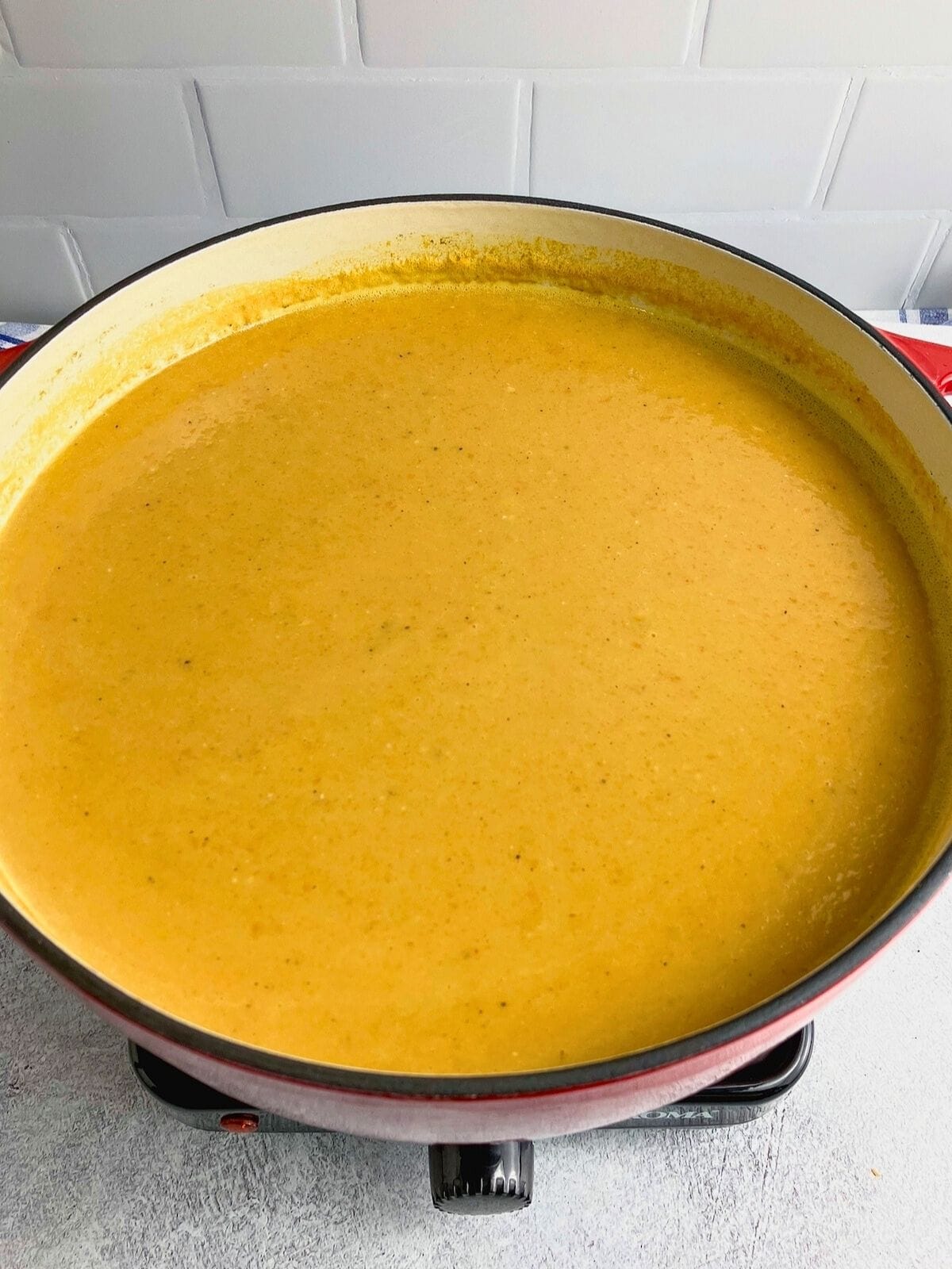 A large red cast iron pot filled with creamy sweet potato carrot soup.