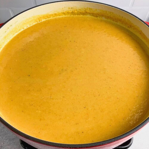 A large red cast iron pot of pureed sweet potato carrot soup.