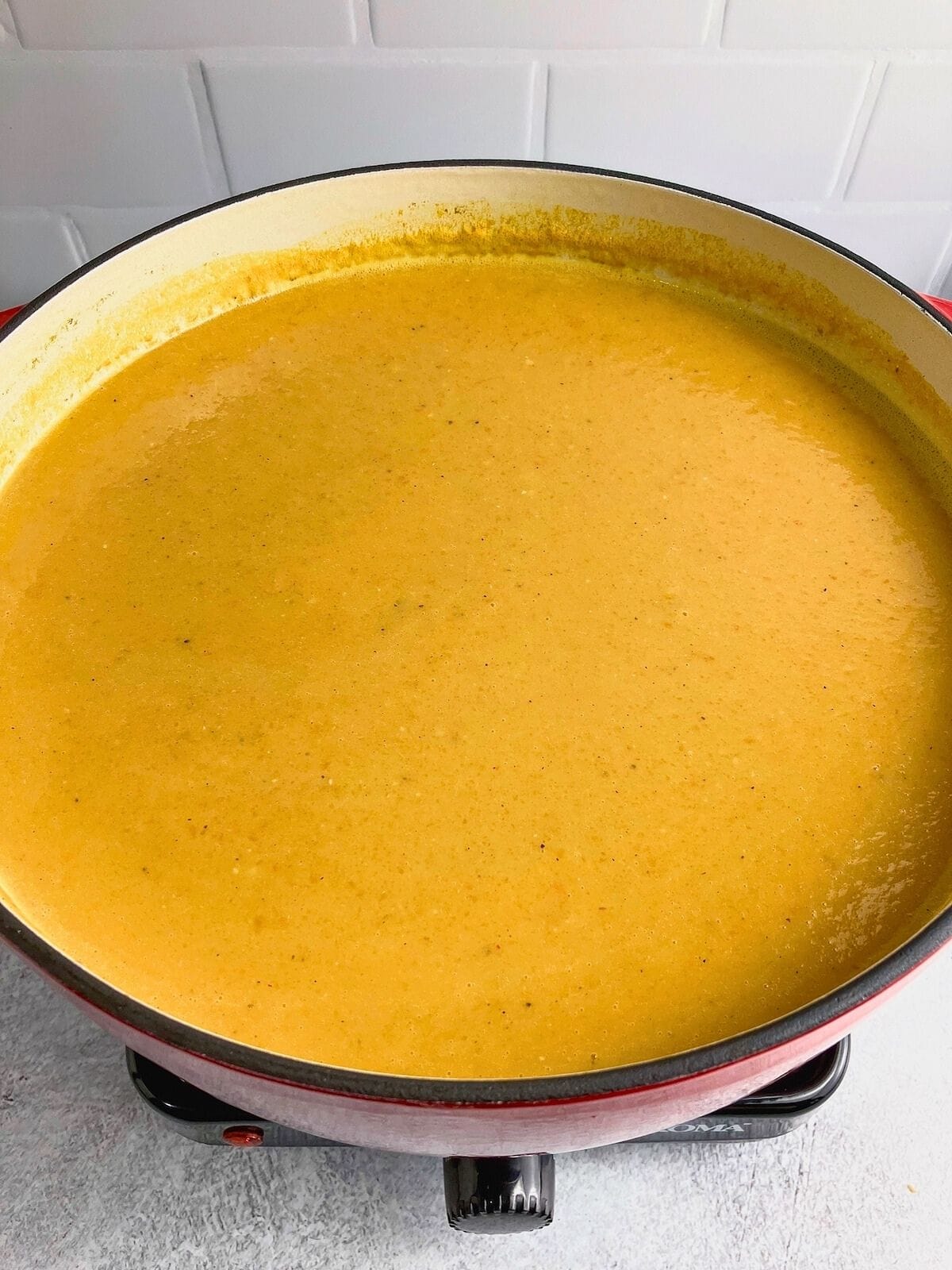 A large red cast iron pot of pureed sweet potato carrot soup.