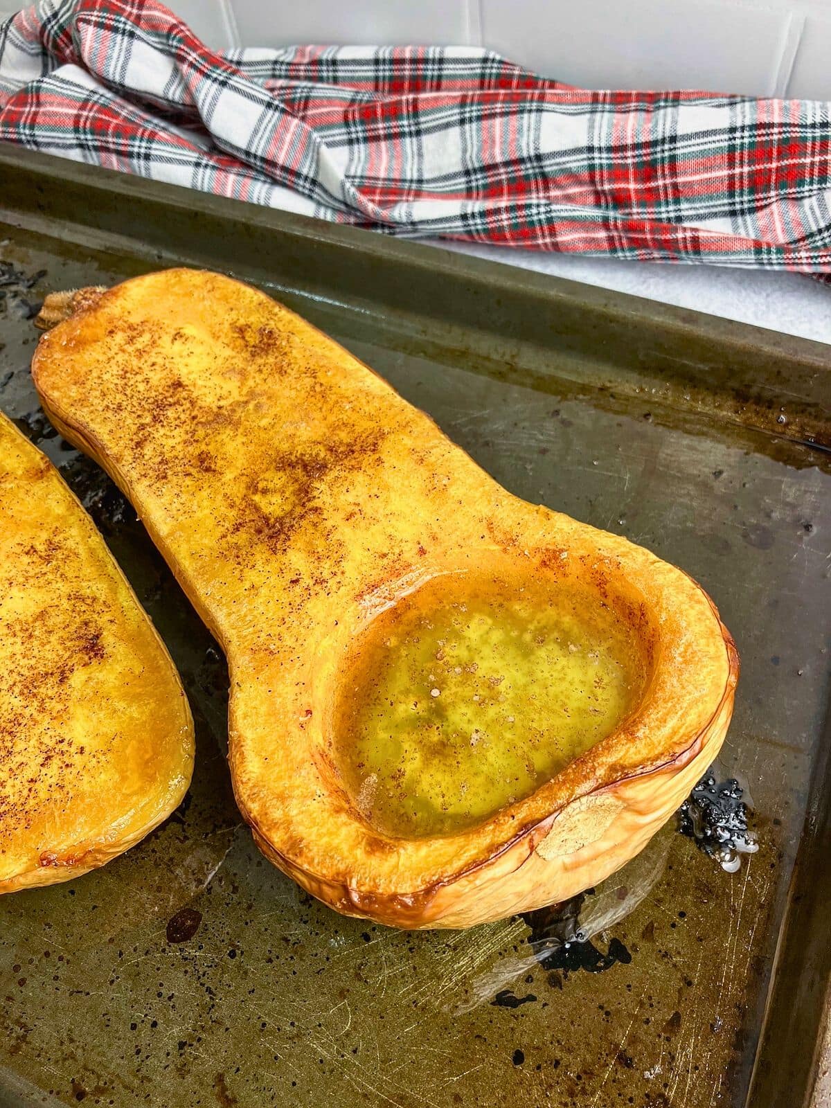 Whole roasted butternut squash with maple syrup, cinnamon, and brown sugar on a baking sheet.