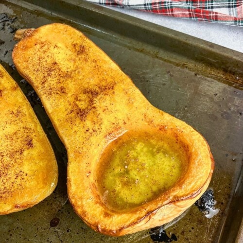 Whole baked butternut squash with maple syrup, cinnamon, and brown sugar on a baking sheet.