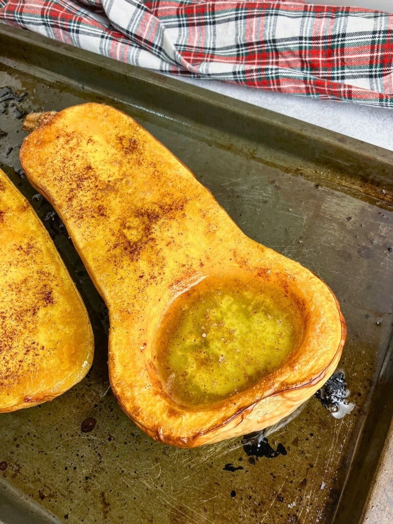 Whole baked butternut squash with maple syrup, cinnamon, and brown sugar on a baking sheet.