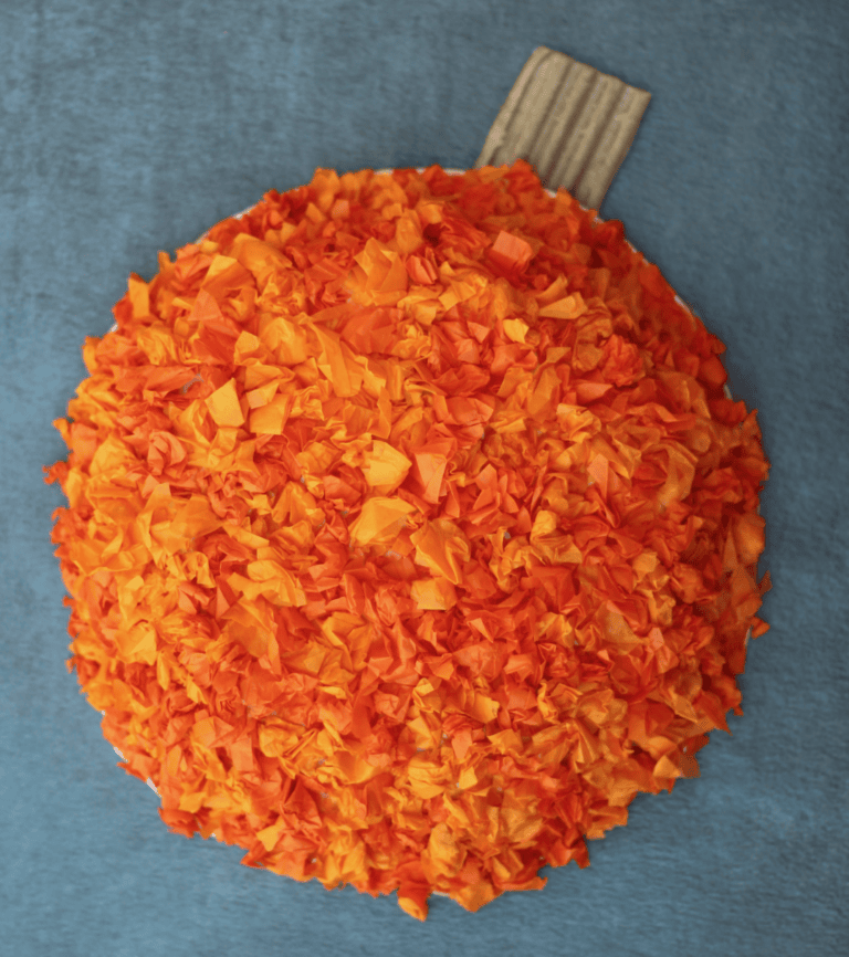 A cute tissue paper pumpkin craft for kids with the pumpkin laying on the table.