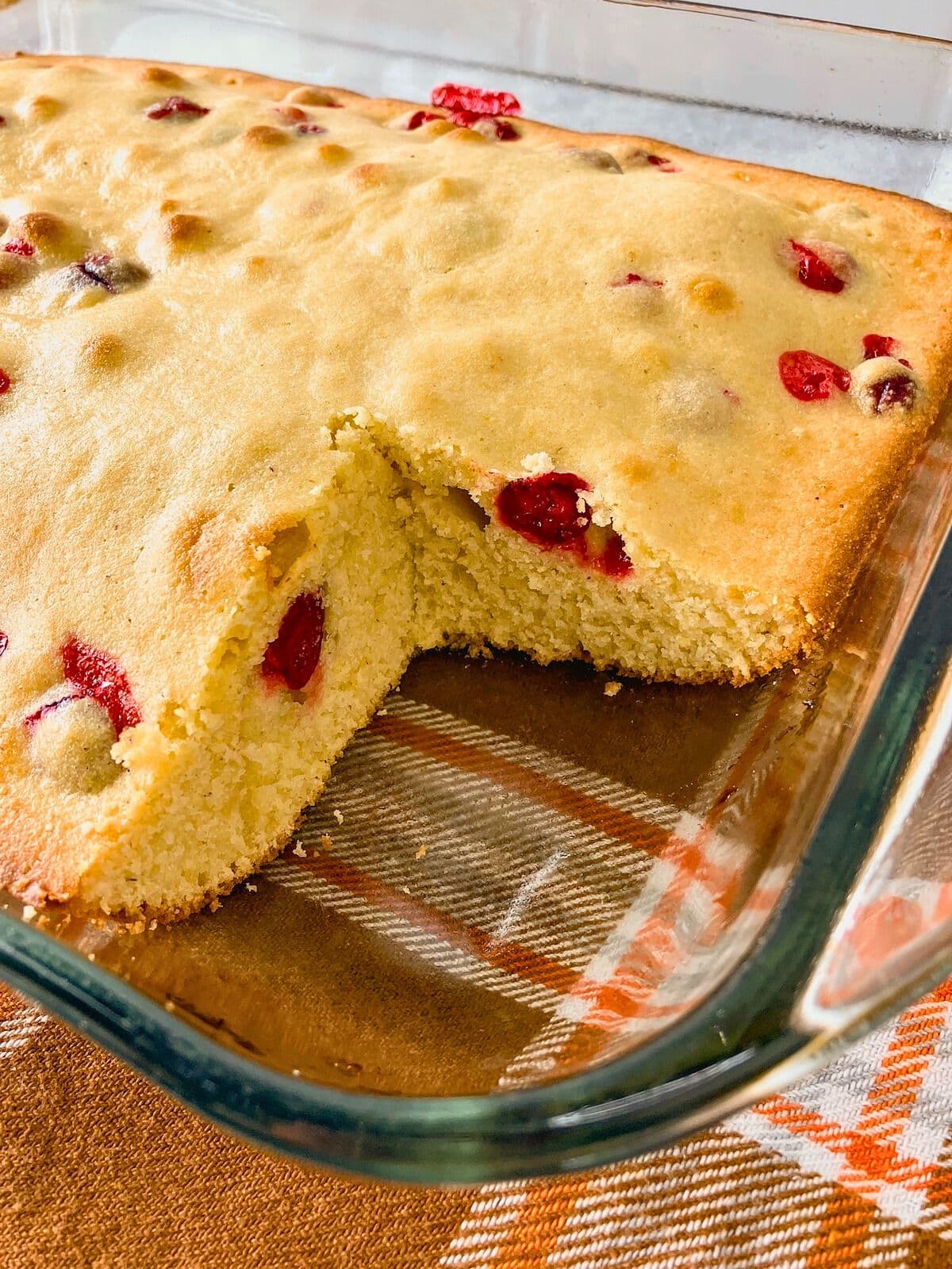 A baking dish of cornbread with cranberries with a slice removed from the pan.