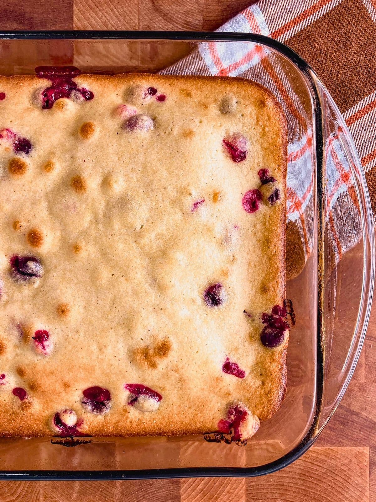 A glass baking dish of warm cranberry cornbread sitting on a wooden counter.