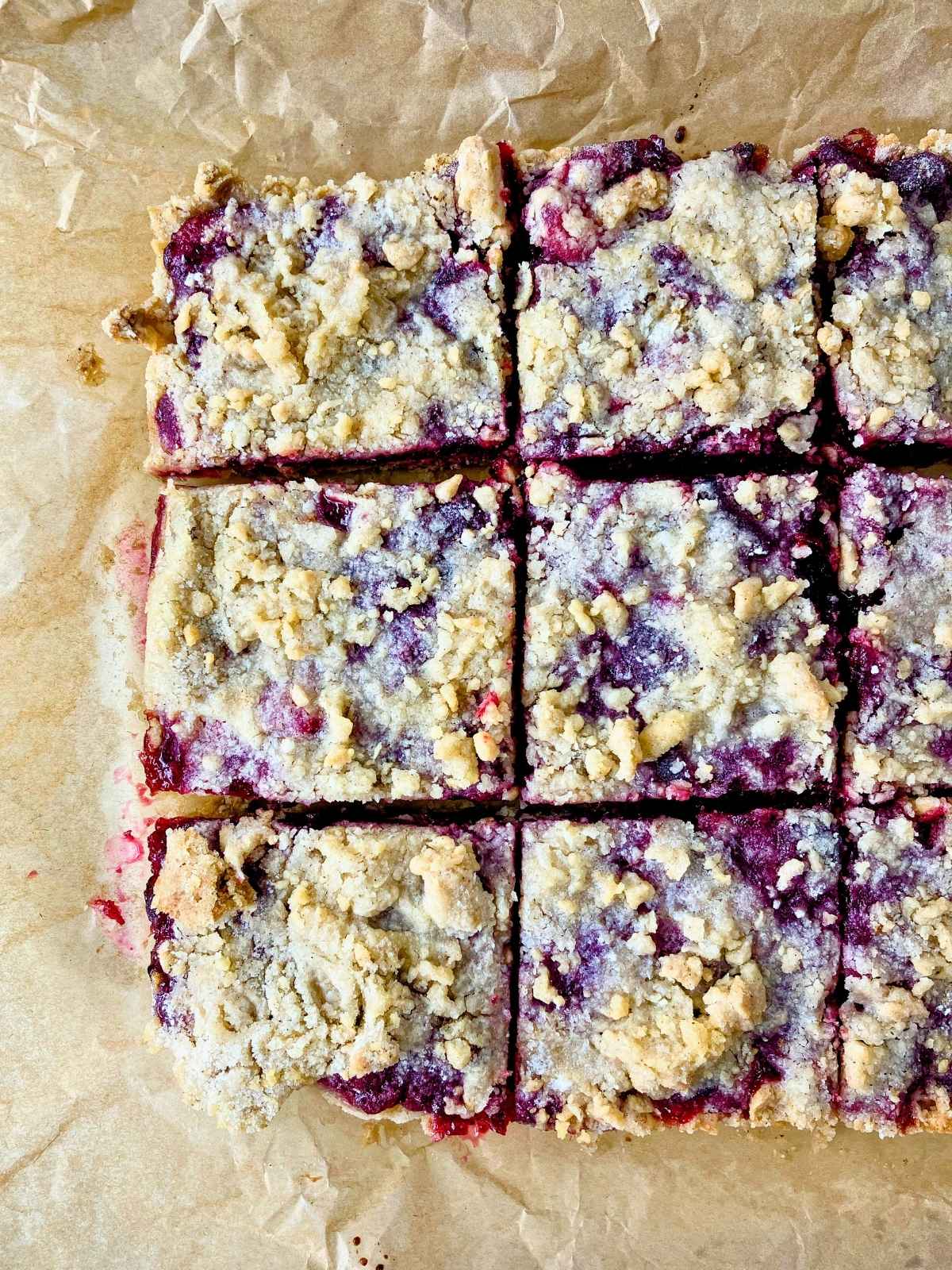 Cooled cranberry crumb bars cut into squares on top of the parchment paper.