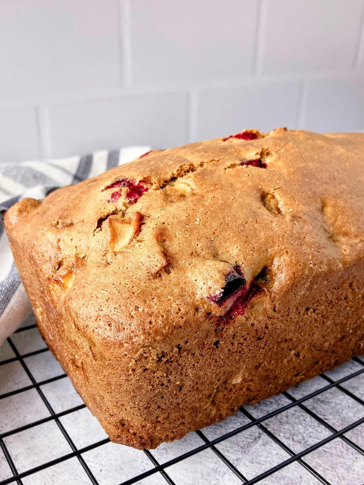A loaf of apple cranberry bread cooling on a wire rack.