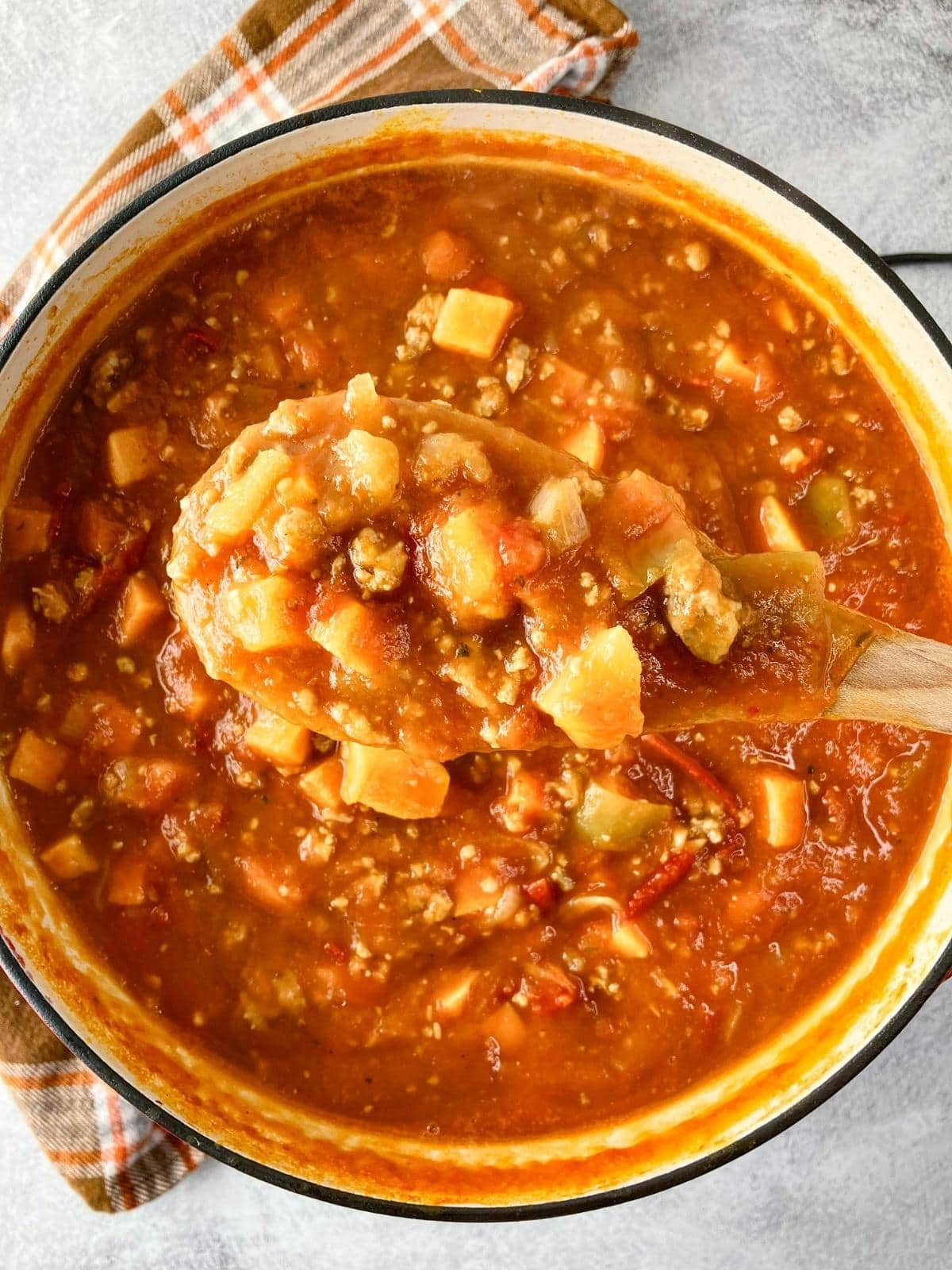 Holding a spoonful of pumpkin sweet potato chili up over the pot.