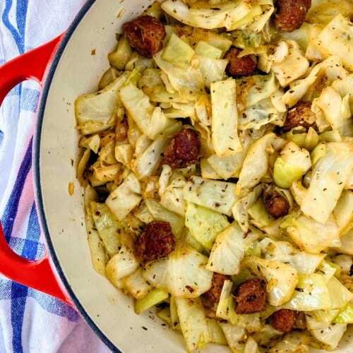 A large red Dutch oven of homemade fried cabbage with sausage and onions.