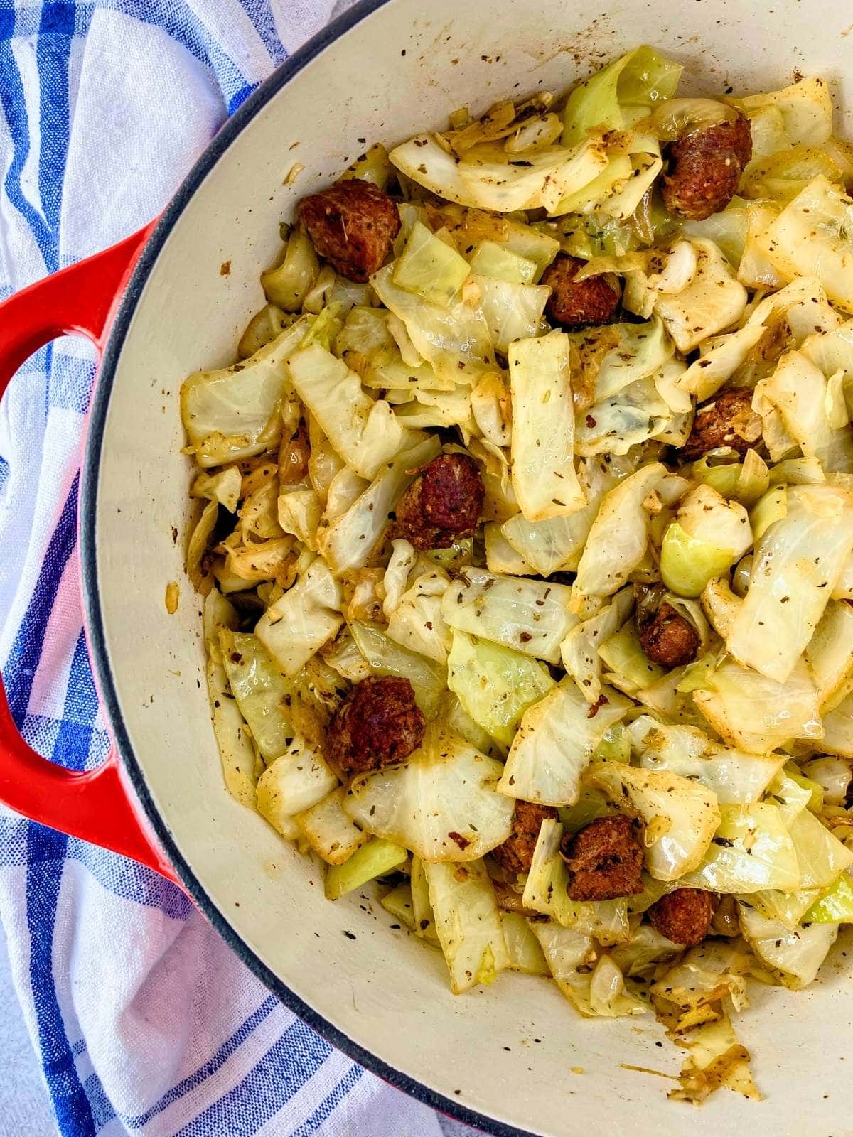 A large red Dutch oven of homemade fried cabbage with sausage and onions.