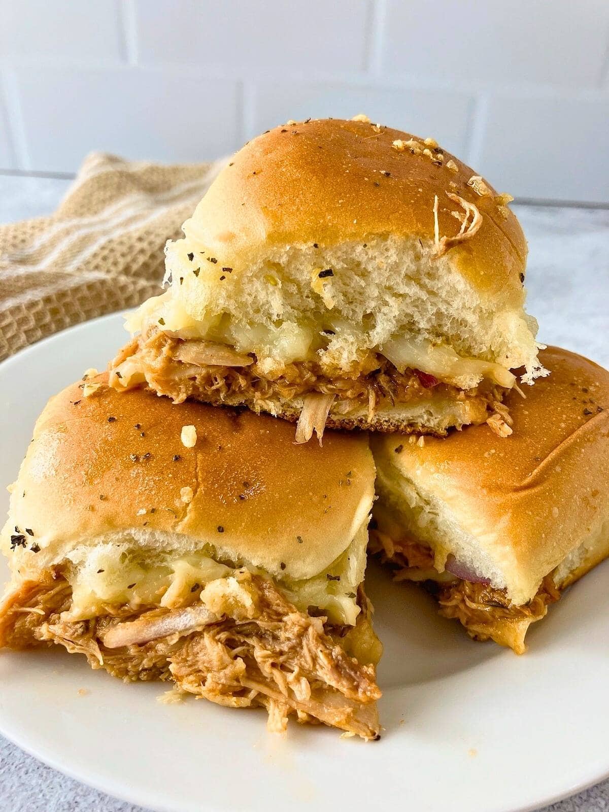 BBQ chicken sliders stacked on a white plate.