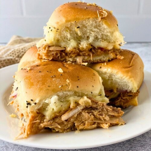 BBQ chicken sliders stacked on a white plate.