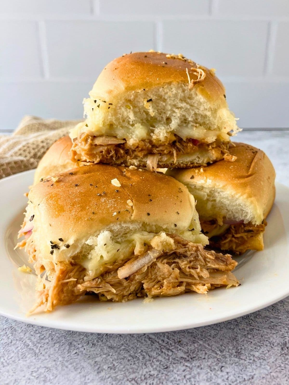 BBQ chicken sliders stacked on a white plate.