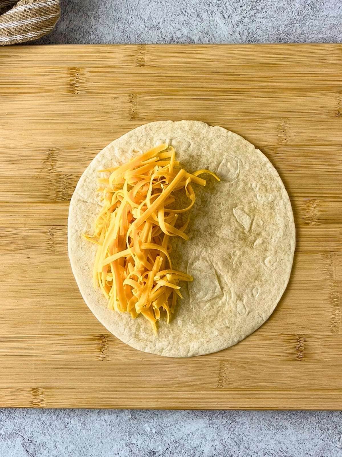 A layer of shredded cheddar cheese was spread on half of the tortilla.