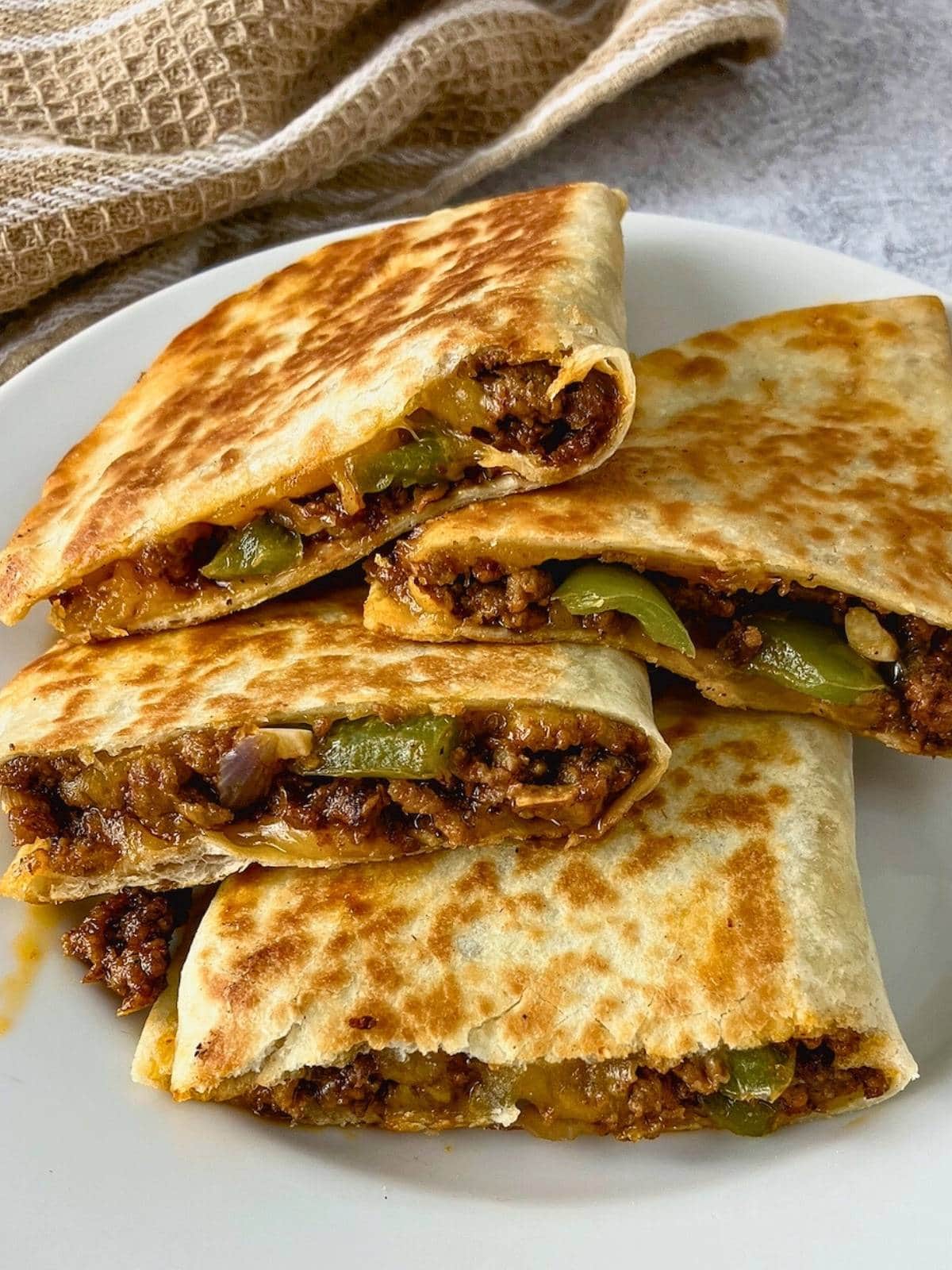 Beef quesadillas made with seasoned ground beef, red onion, green peppers, and cheese sliced and stacked on a plate.